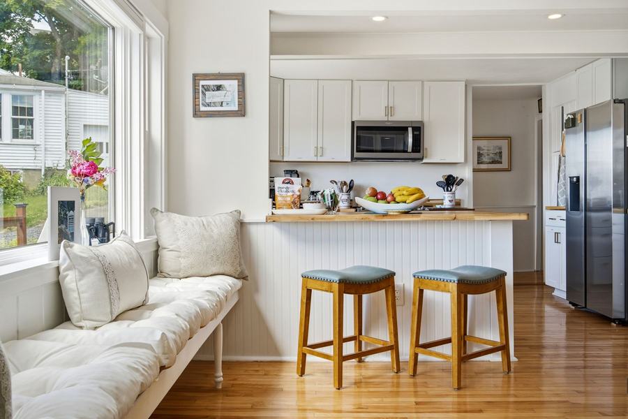 Shared guest kitchen at Greenleaf Inn with full-size refrigerator, microwave, breakfast counter, stools, and window seating, available to all guests.